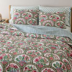 a bed with a green and pink quilt on top of it next to a night stand