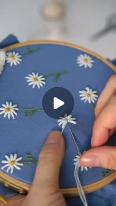 someone is stitching daisies on a blue cloth