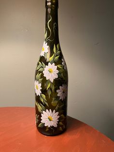 a bottle with flowers painted on it sitting on a red table next to a gray wall