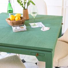 a bowl of lemons sits on a green table next to two chairs and a vase with flowers