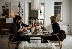 three people sitting at a table with food in front of them and candles on the wall