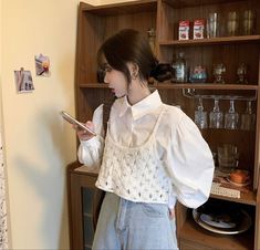 a woman standing in front of a wooden shelf holding a cell phone and looking at it