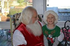 an old man sitting next to a little boy wearing a santa clause hat and green shirt