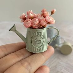 a miniature watering can with pink flowers in it's handle is held by a hand