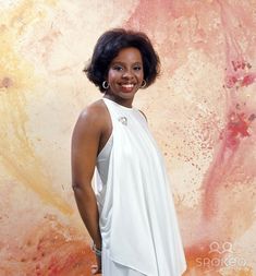 a woman standing in front of a painting wearing a white dress and smiling at the camera