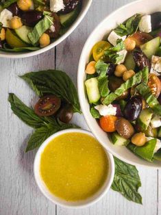 two bowls filled with salad and dressing on top of a white wooden table next to each other