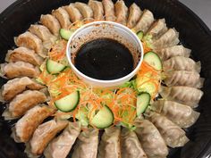 a black plate topped with dumplings and cucumbers next to a dipping sauce