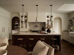 a large kitchen with white cabinets and wooden flooring is pictured in this image, there are three stools at the center of the island