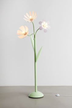 a green vase with three flowers in it on a table next to a white wall