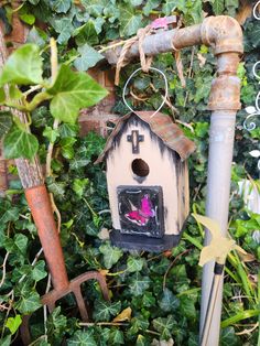 a birdhouse hanging from the side of a pole in front of some bushes and plants