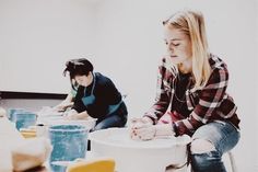 two women are sitting at a table making bowls