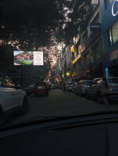 cars are parked on the street in front of tall buildings and trees, with one person walking down the sidewalk