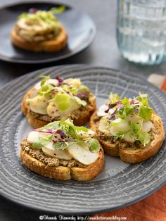 three sandwiches with lettuce and other toppings sit on a plate next to a glass of water