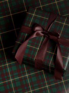 a green and red plaid wrapping paper with a brown ribbon on the top is wrapped in a gift box