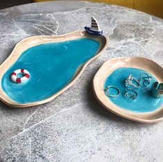 two small trays with rings on them sitting on top of a marble table next to each other