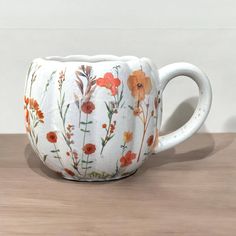 a white coffee cup with orange and red flowers painted on the inside is sitting on a wooden table