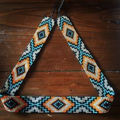 a colorful beaded necklace hanging on a wooden surface with beads in the shape of an triangle