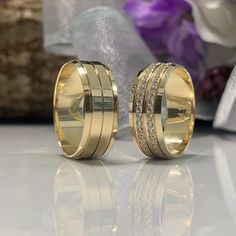 two gold wedding rings with diamonds on them, sitting next to a bouquet of flowers