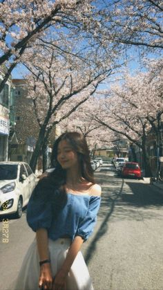 a woman is walking down the street with cherry blossoms on trees in front of her