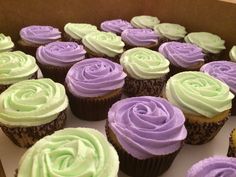 there are many cupcakes in the box with frosting on them and one is purple and green