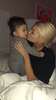 a woman kissing a small child on top of a bed