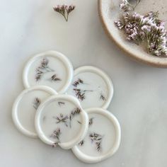 four white plates with dried flowers on them next to a bowl and planter in the background