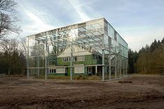 a large glass building sitting in the middle of a dirt field next to a forest