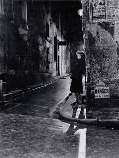 an old black and white photo of a woman leaning against a street sign in the rain