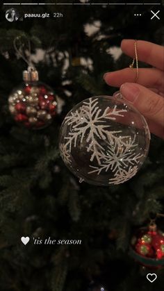 a hand holding a glass ornament with snowflakes on it in front of a christmas tree