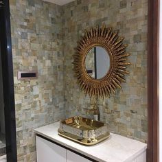 a bathroom with a sink, mirror and tiled wall behind the counter top in gold