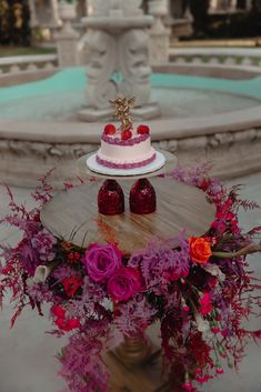 there is a cake on the table with flowers and strawberries in front of it