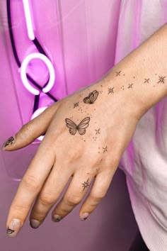 a woman's hand with stars and butterflies tattoo on her left wrist, in front of a pink neon light