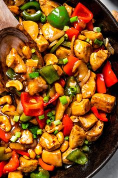 a skillet filled with chicken, peppers, and green peppers next to a wooden spoon