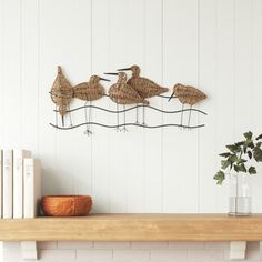 three birds sitting on top of a wooden shelf next to a vase and bookcase