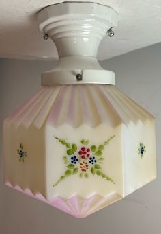 a white light fixture with flowers painted on it's side and an attached lamp shade