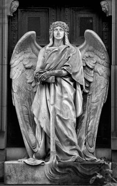 an angel statue is standing in front of a door with his arms crossed and hands folded