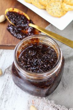 a jar of jam sitting on top of a table next to crackers and nuts