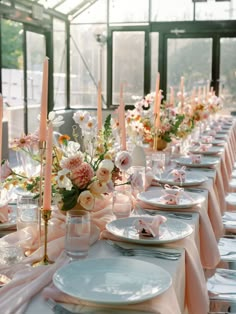 a long table set with plates and candles for an elegant wedding reception in a greenhouse