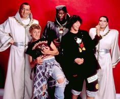 a group of people standing next to each other in front of a red wall wearing costumes