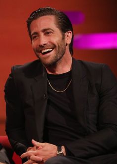 a smiling man in a black suit sitting on a red chair