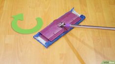 a purple mop on top of a wooden floor next to a green circle with an arrow