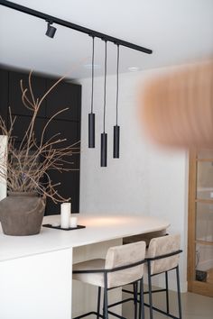 a white table with some chairs and a vase on it next to two black lights that are hanging from the ceiling