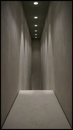 an empty hallway with white walls and light at the end is lit by recessed lights