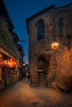 an alley way with stone buildings and lanterns hanging from the side of it at night