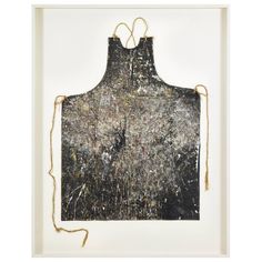 an apron hanging on a string in front of a white frame with paint splattered all over it