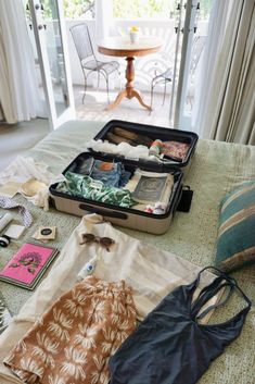 an open suitcase sitting on top of a bed filled with clothing and other items next to a table