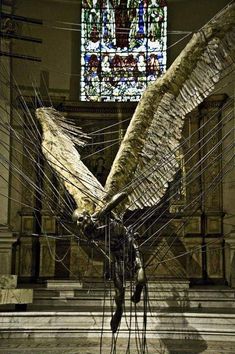 a large bird sculpture in front of a stained glass window with wires running through it