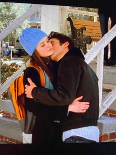 a young man and woman embracing each other in front of a stair case with stairs behind them