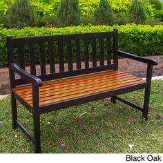 a wooden bench sitting on top of a green grass covered park field next to bushes