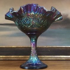 a purple glass vase sitting on top of a wooden table next to a framed painting